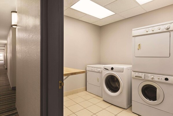 A laundry room with two washing machines, a wooden shelf, and a tiled floor.