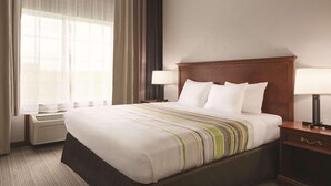 A hotel room with a large bed, two bedside tables with lamps, a window with curtains, and an air conditioning unit.