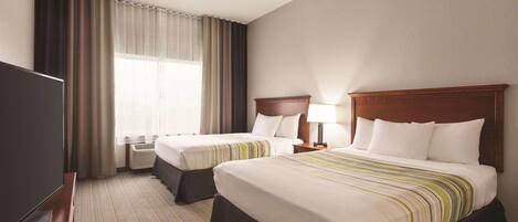 A hotel room with two beds, a TV, and a window with curtains.