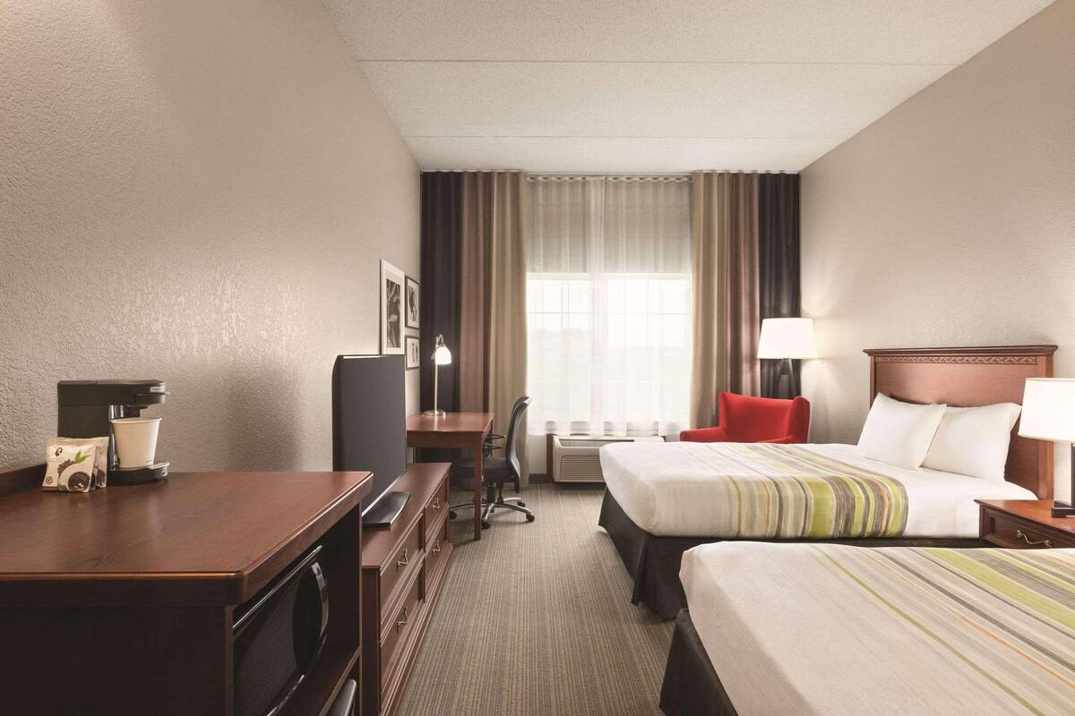 A hotel room with two beds, a desk, a chair, a TV, and a coffee maker.