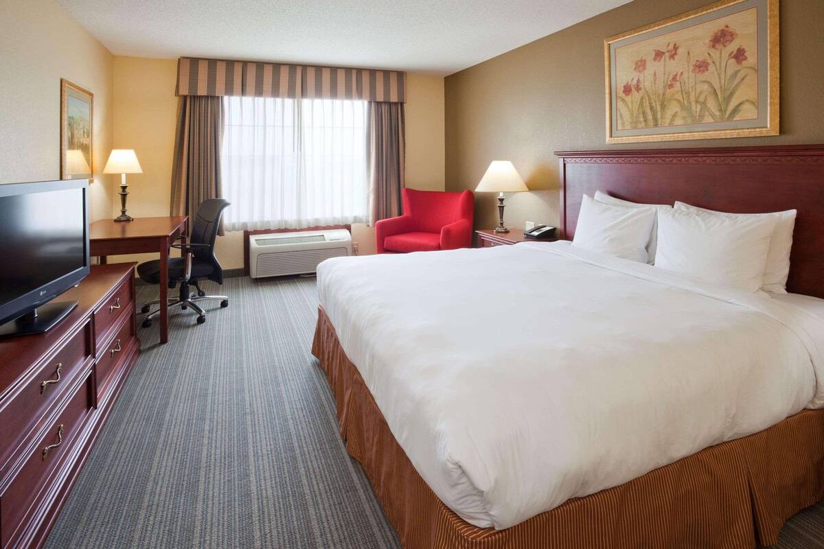 A hotel room with a large bed, a desk with a TV, a chair, and a window with curtains.