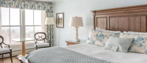 Un dormitorio con una cama grande, un cabecero de madera, una mesita de noche con lámpara, una silla y una ventana con cortinas.