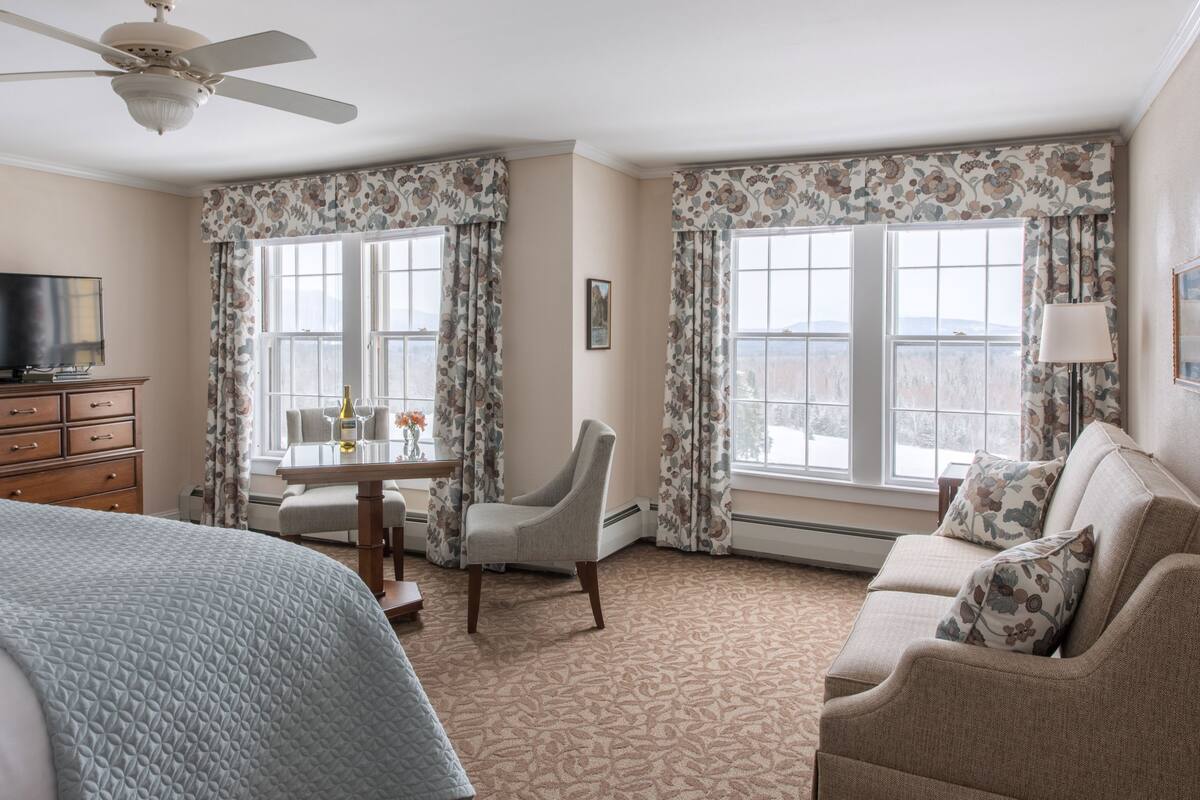 A hotel room with a bed, a desk with a chair, a television, and a sofa.