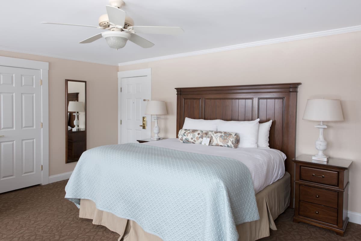 A bedroom with a bed, nightstands, a ceiling fan, and a door.