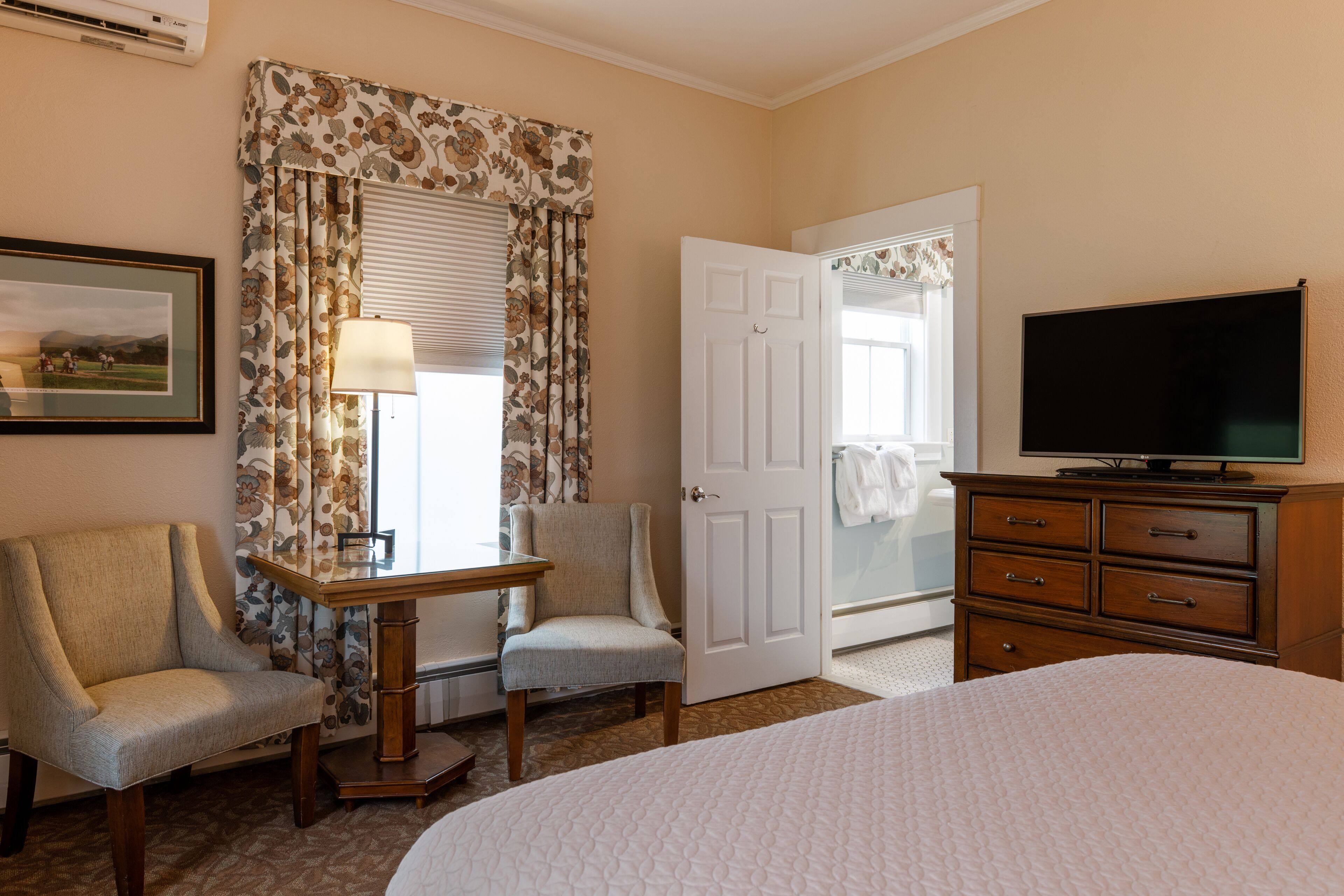 A hotel room with a bed, a desk with a chair, a television, and a wardrobe.