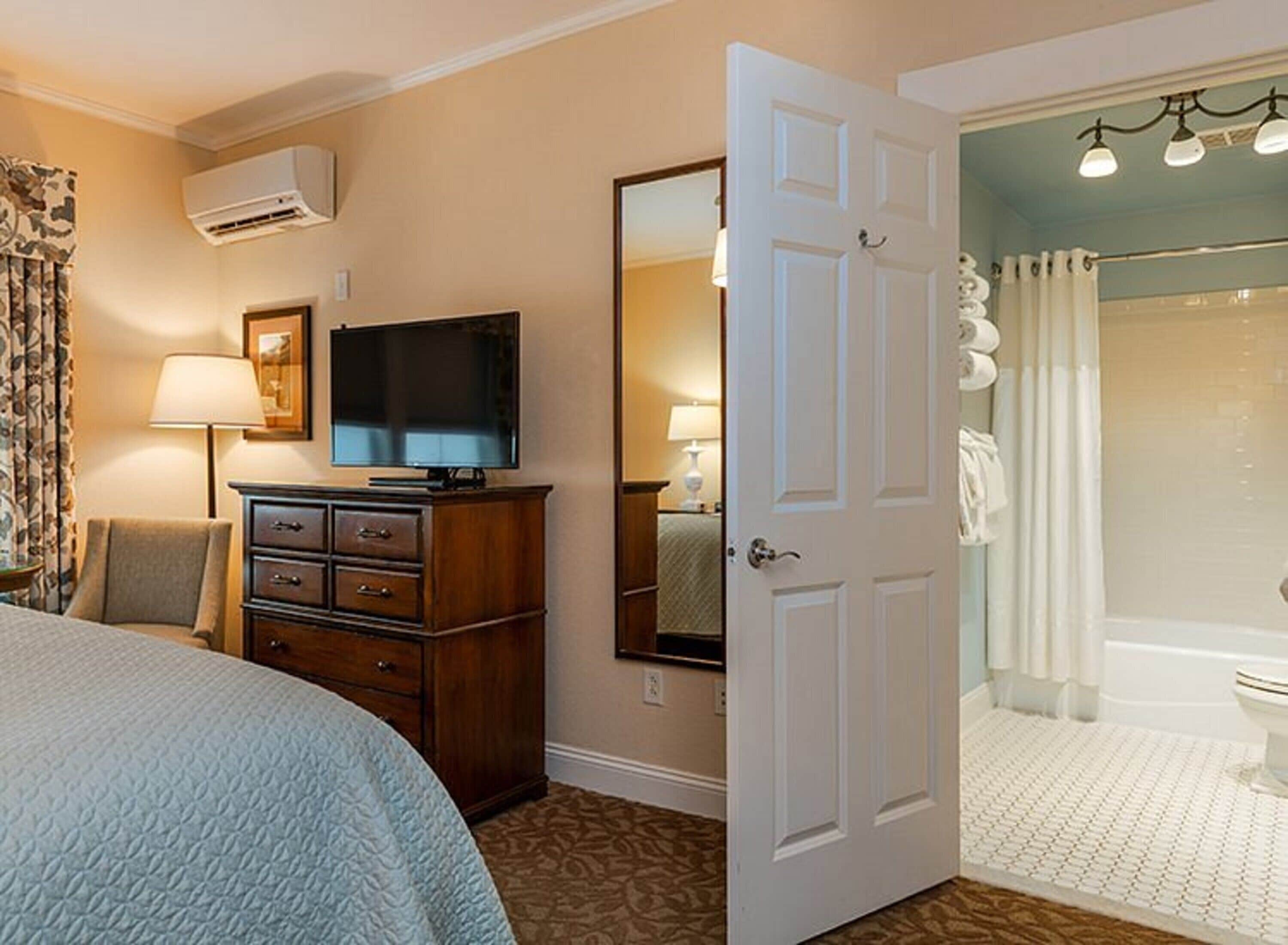 A hotel room with a bed, a television, a dresser, a mirror, and a bathroom with a shower and toilet.