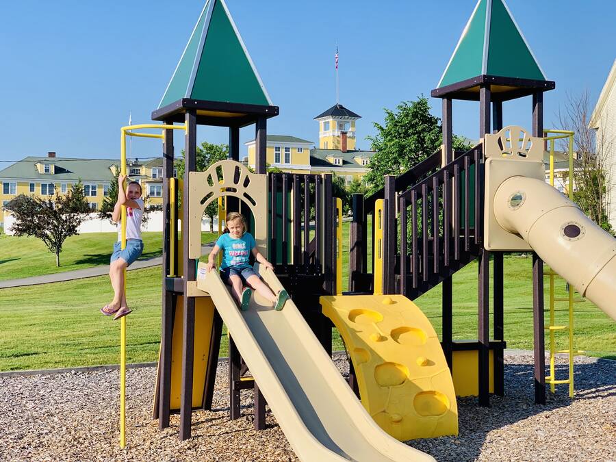 A playground with a slide and climbing structures, surrounded by a well-maintained lawn and residential buildings in the background.