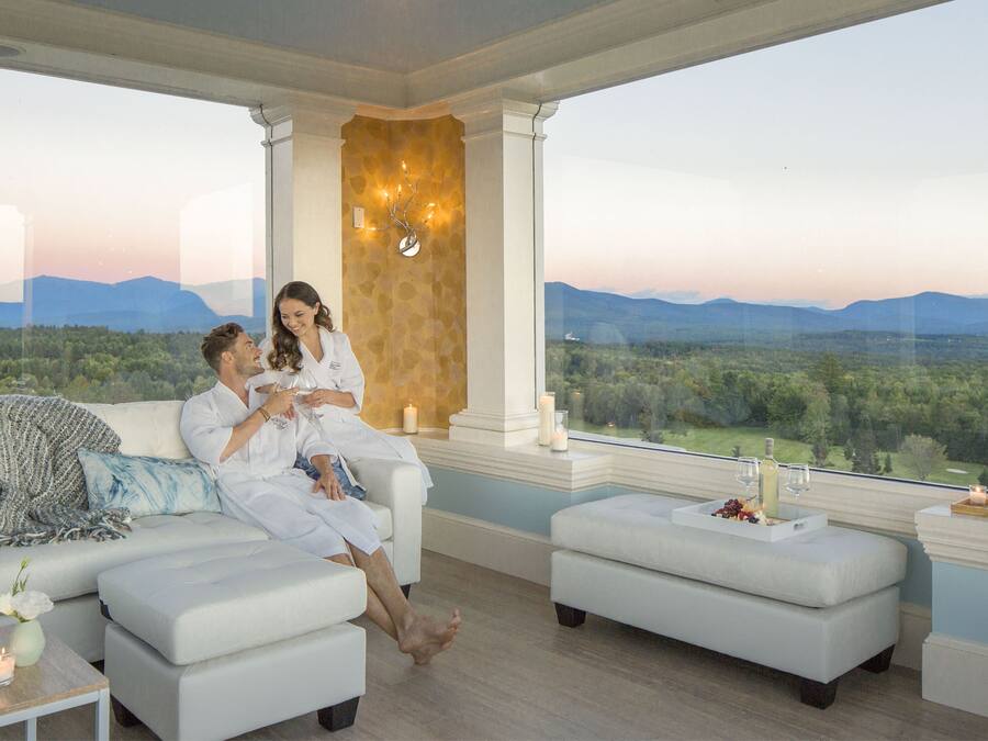 A couple in a modern, well-lit room with a large window overlooking a scenic landscape.