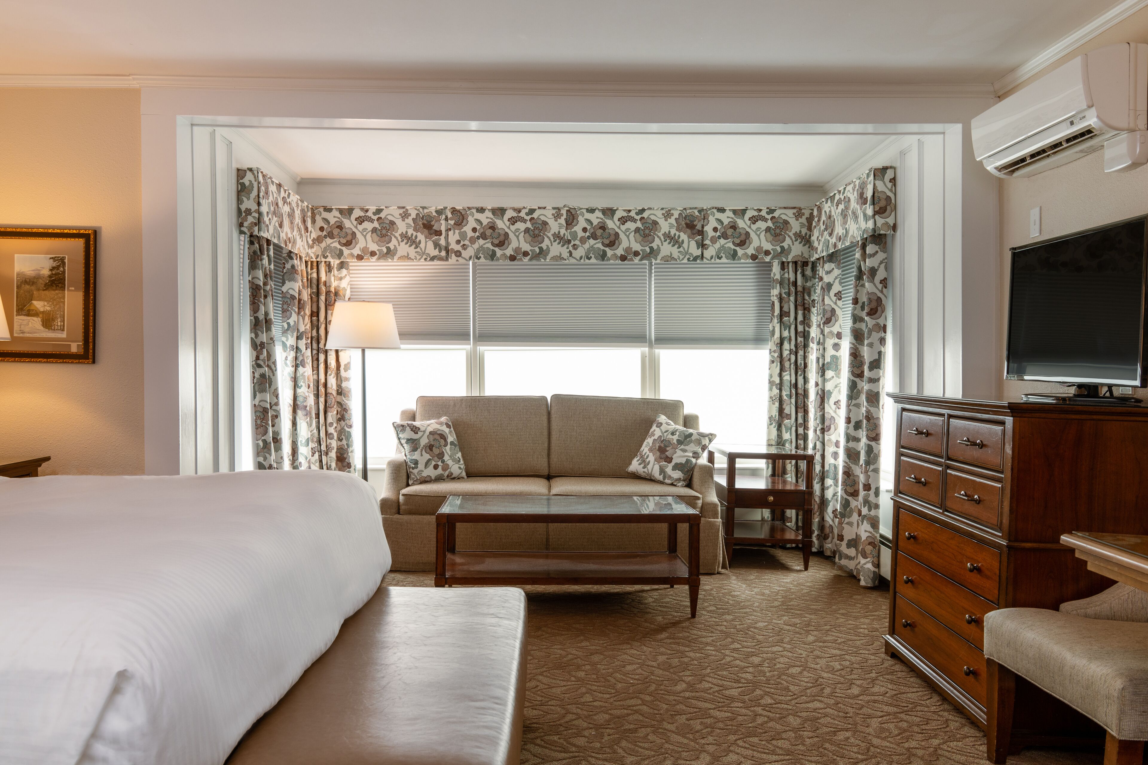 A hotel room with a large bed, a sofa, a coffee table, a dresser, and a television.