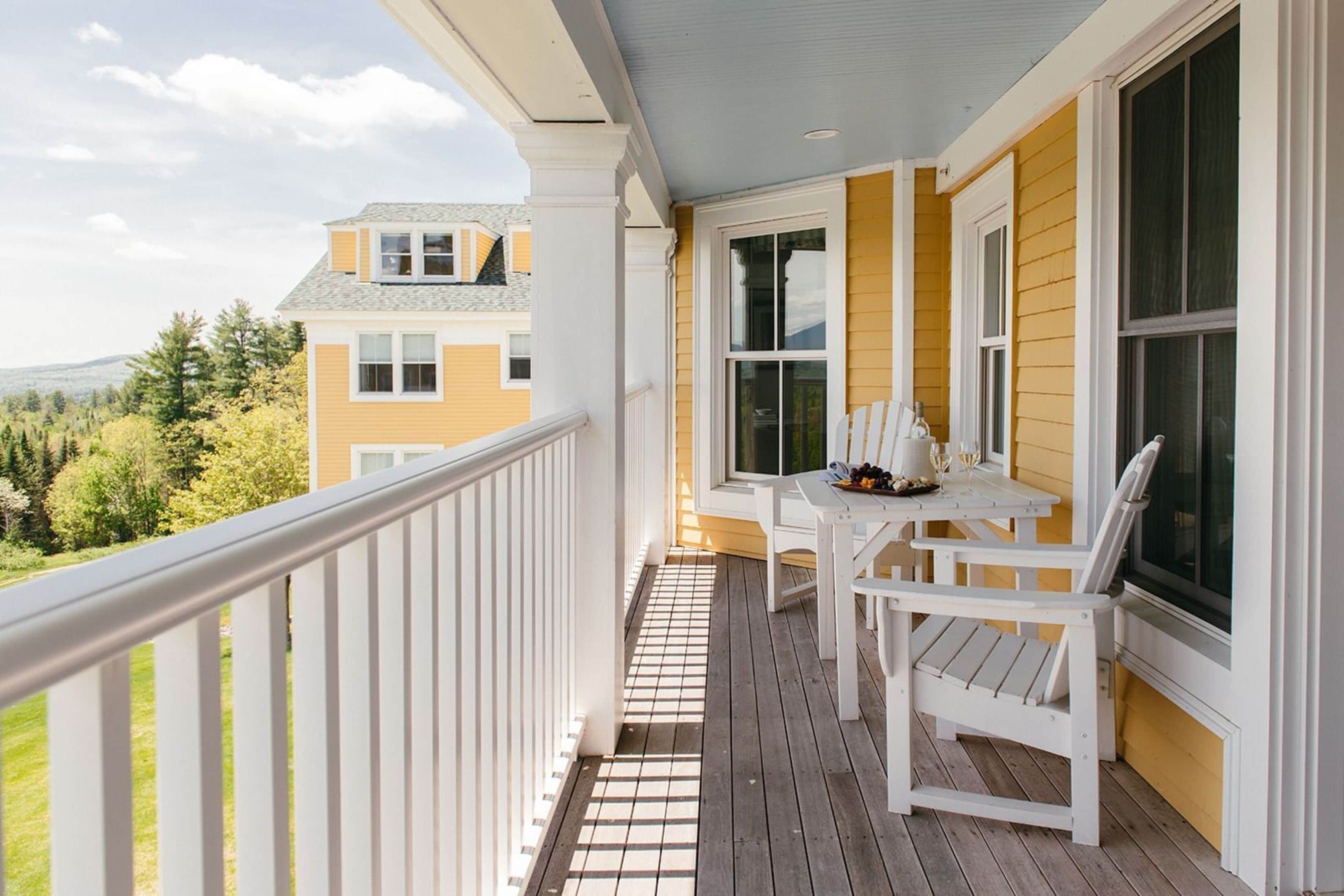 Un balcon avec une balustrade blanche, une table avec des chaises et une vue sur un immeuble jaune et des arbres.