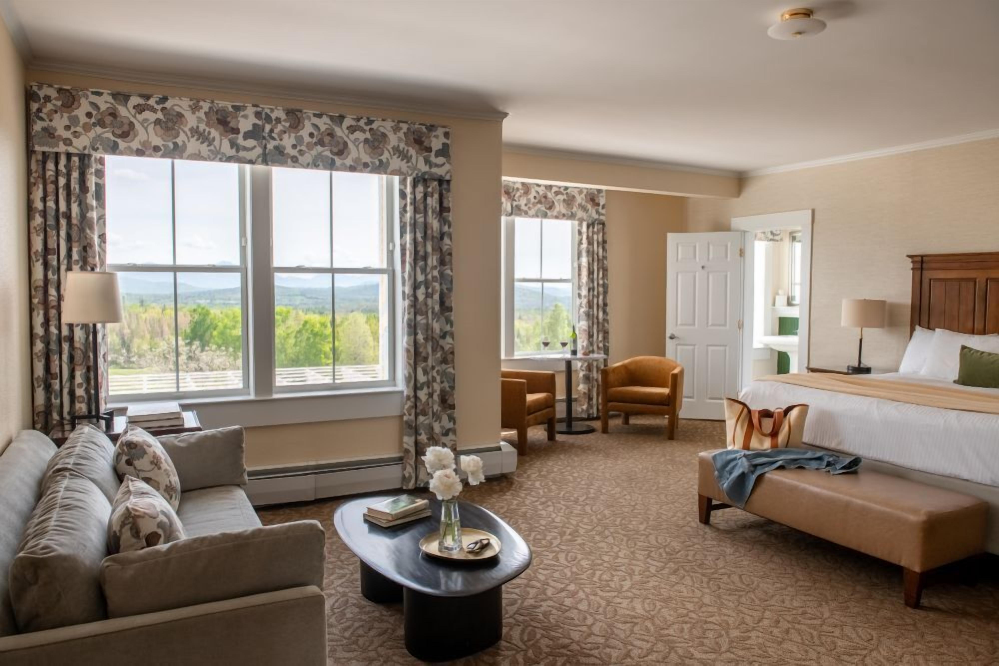 A hotel room with a bed, a sofa, a dining table, and a view of the outdoors.