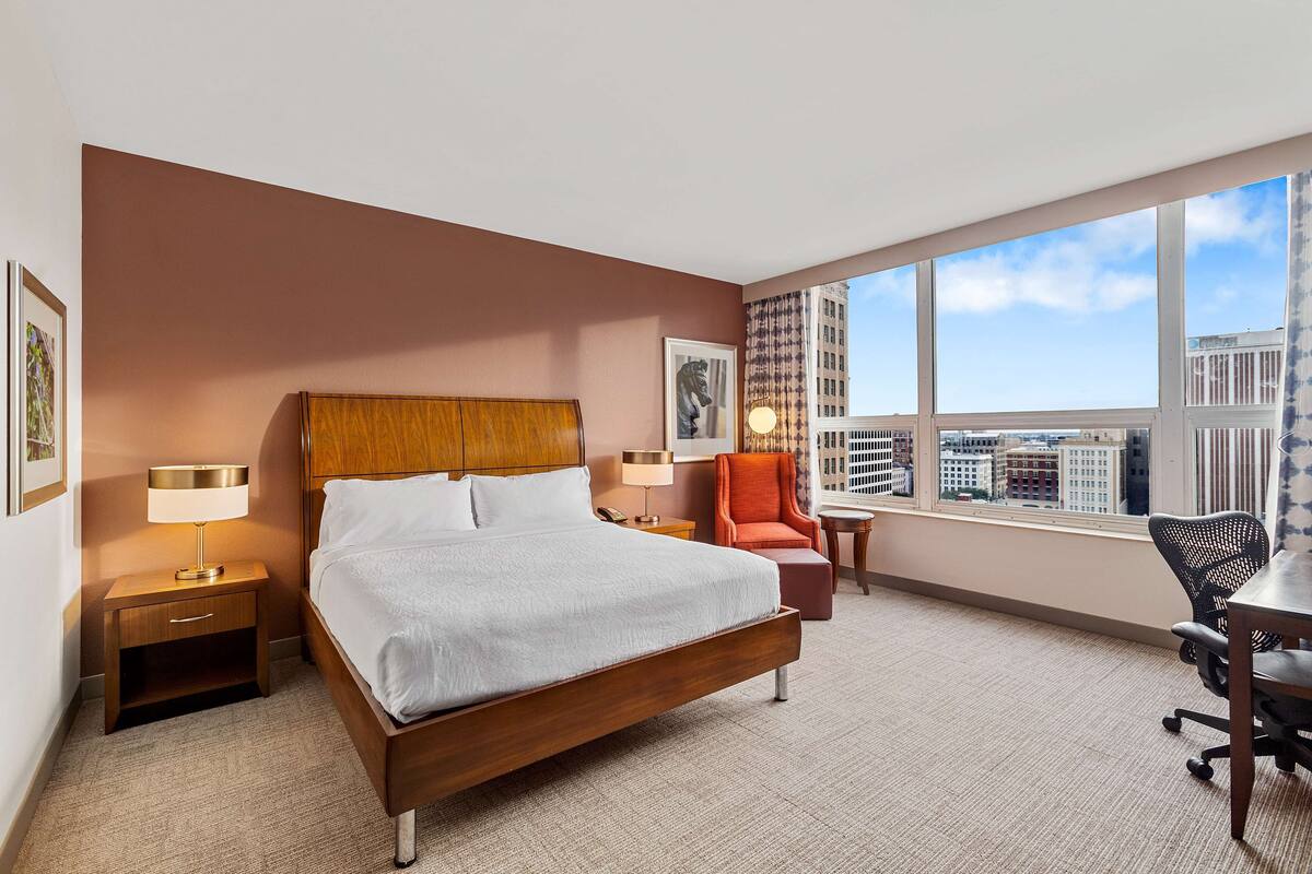 Habitación de hotel con una cama grande, un escritorio, una silla y vistas a la ciudad.