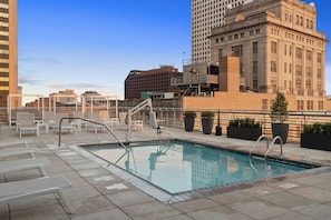 Una piscina en la azotea con sillones de descanso y vistas a edificios de la ciudad.