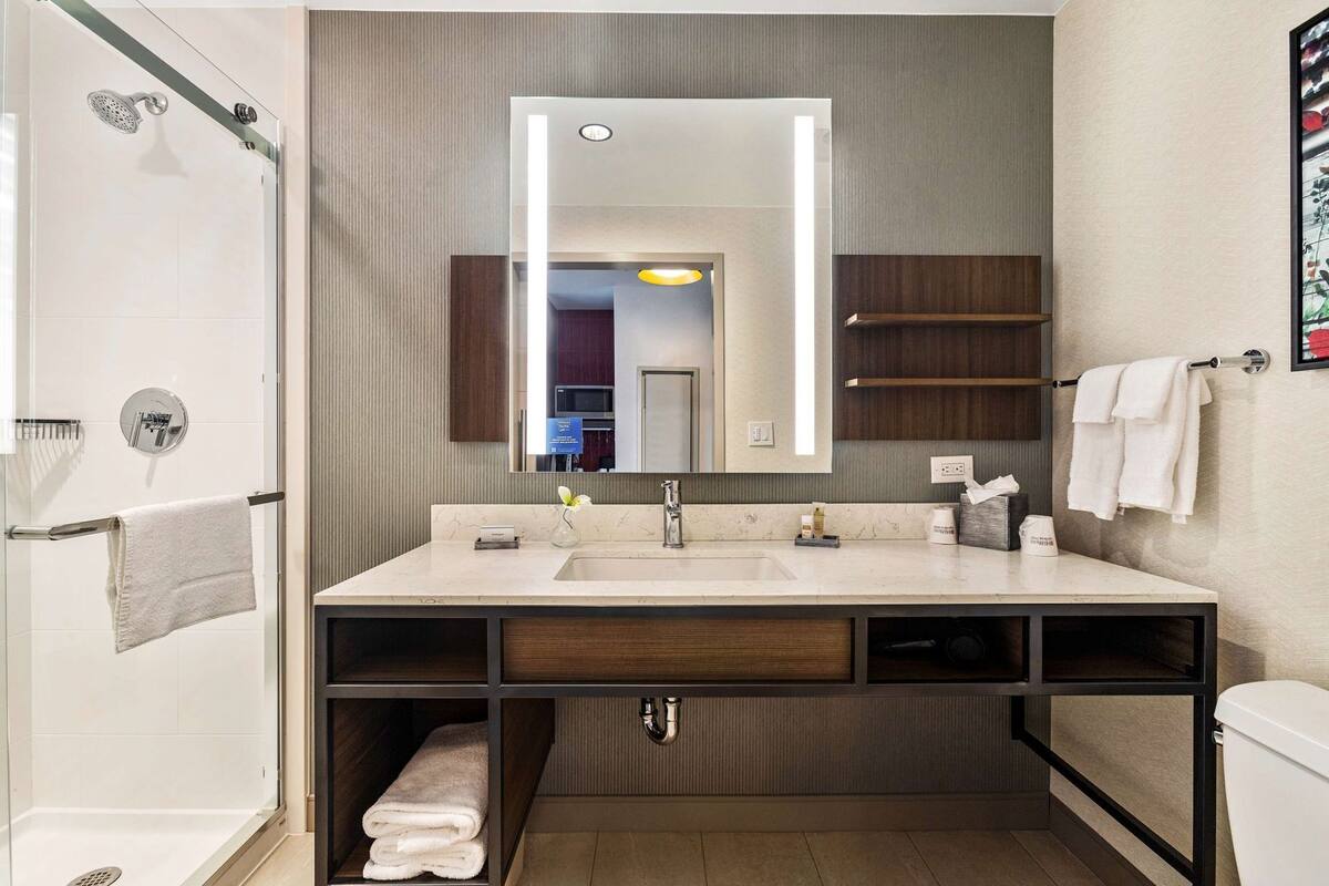 Un baño moderno con cabina de ducha de vidrio, un espejo grande, un lavabo con tocador y un inodoro.