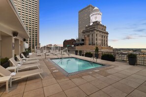 Una piscina en la azotea con sillones de descanso, vista panorámica de la ciudad y un edificio grande con una cúpula.
