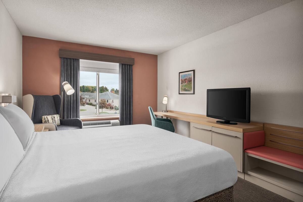 A hotel room with a large bed, a desk with a television, a chair, and a window with curtains.