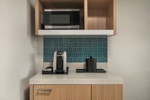 A kitchen with a microwave, coffee maker, and a kettle on the countertop.