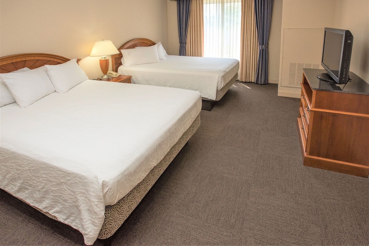 A hotel room with two beds, a desk with a television, and a window with curtains.