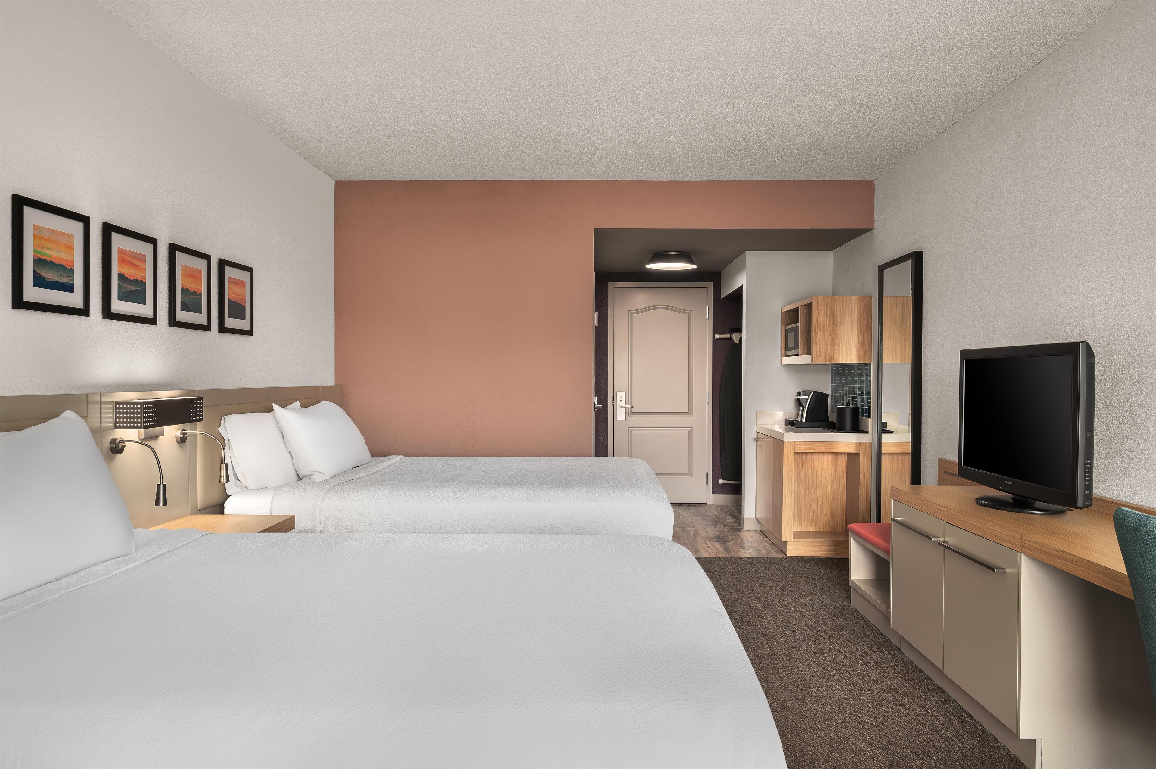 A hotel room with two beds, a desk with a television, a bathroom, and a hallway.