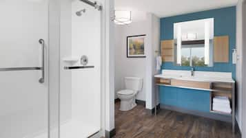 A modern bathroom with a glass shower enclosure, a white toilet, a vanity with a mirror, and a blue accent wall.