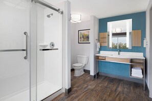 A modern bathroom with a glass shower enclosure, a white toilet, a vanity with a mirror, and a blue accent wall. - Hilton Garden Inn Wooster (Wooster)