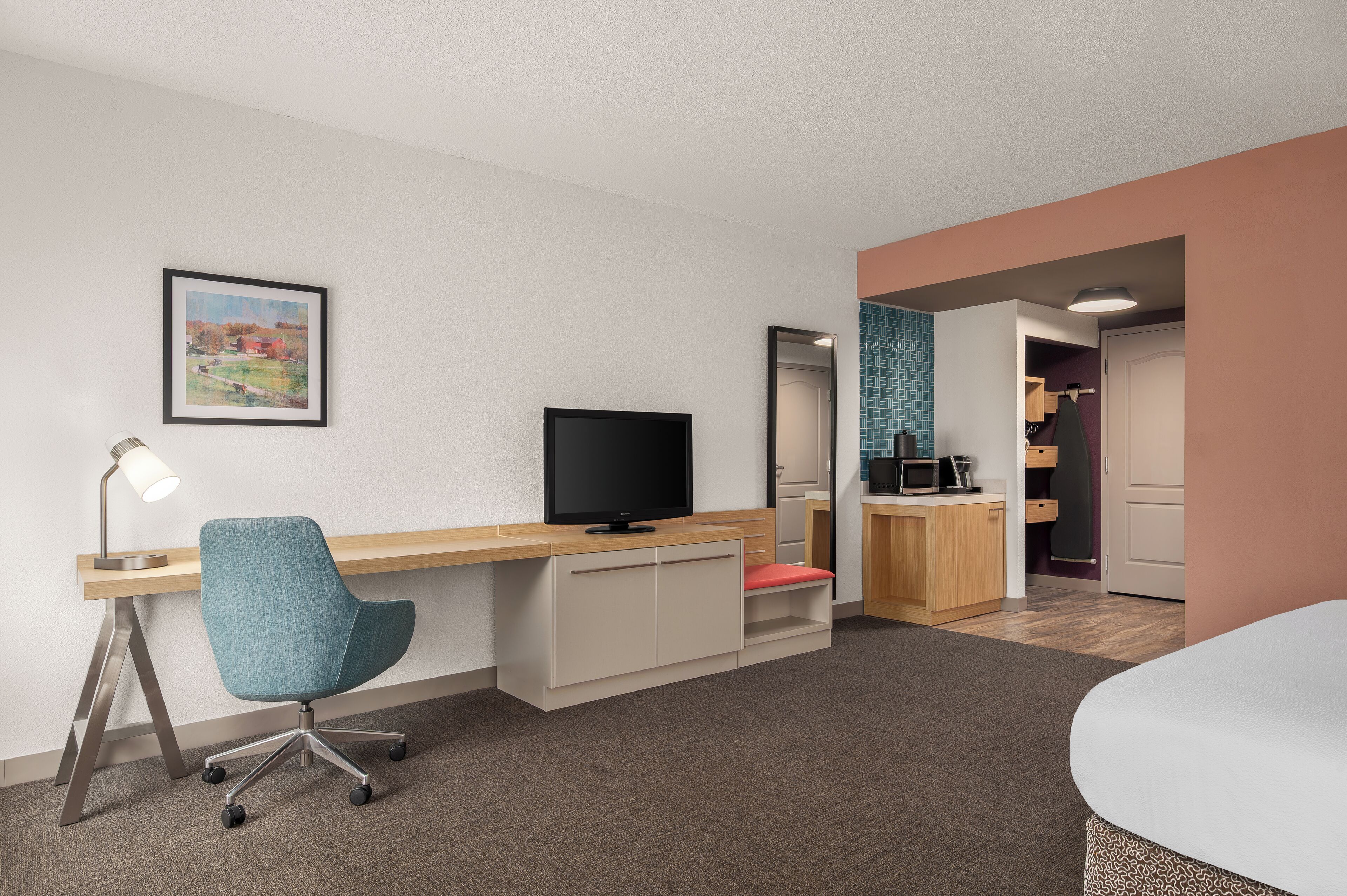 A hotel room with a desk, chair, TV, and a bed.