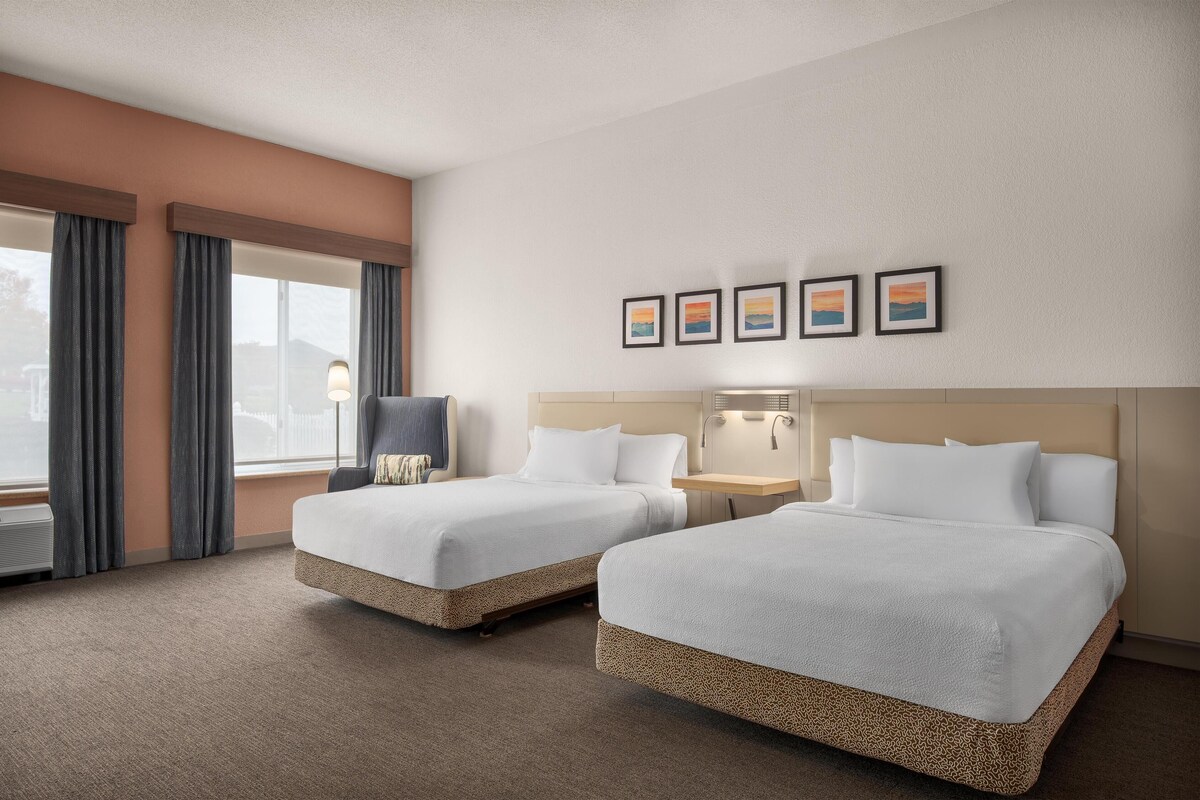 A hotel room with two beds, a nightstand, a lamp, and a wall-mounted picture.