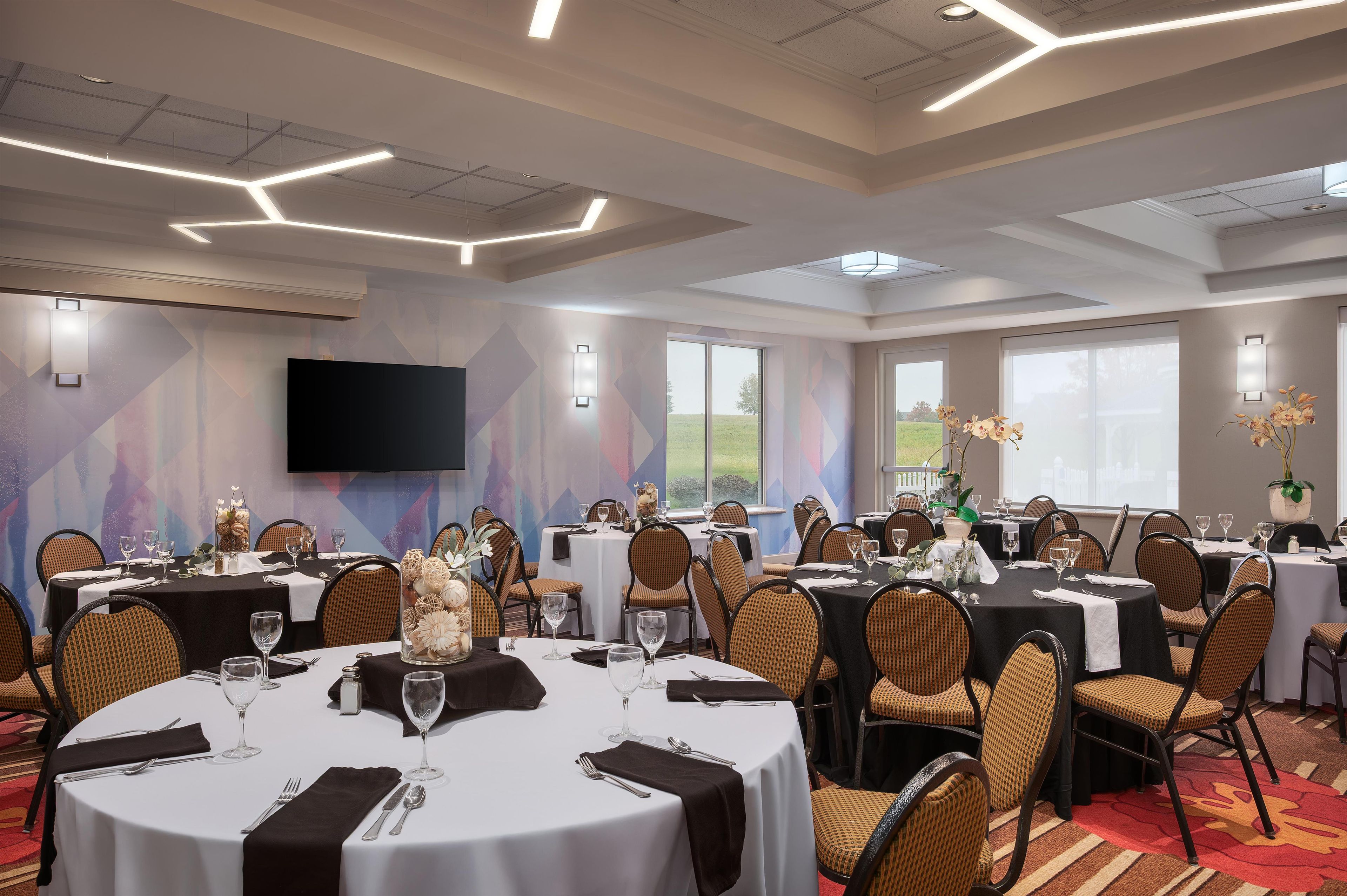 A conference room with multiple round tables, chairs, and a flat-screen TV mounted on the wall.