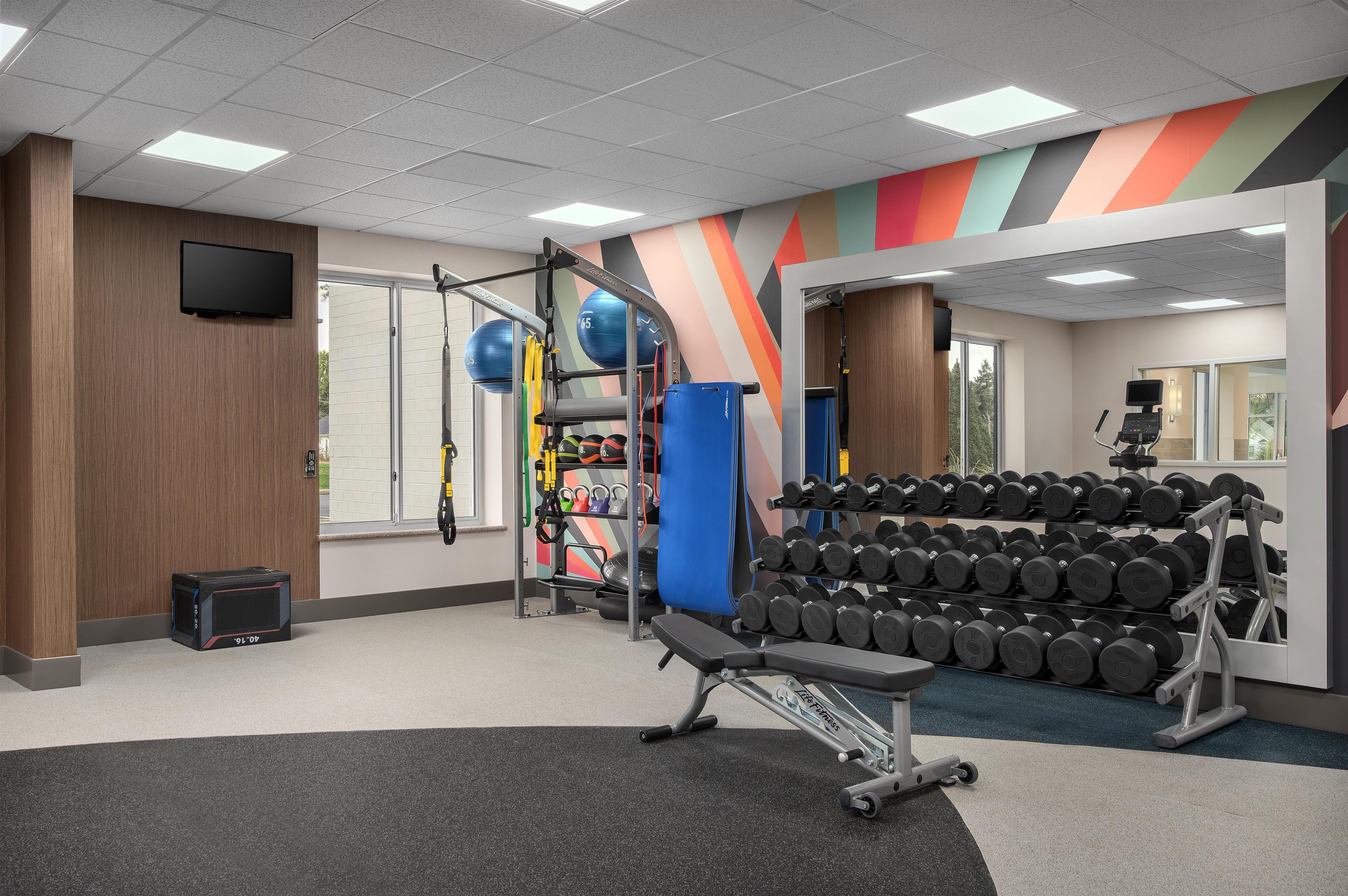 Ein Fitnessstudio mit Trainingsgeräten, Gewichtsständern und einem Fernseher an der Wand.