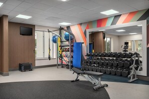 A gym with exercise equipment, weight racks, and a television on the wall.