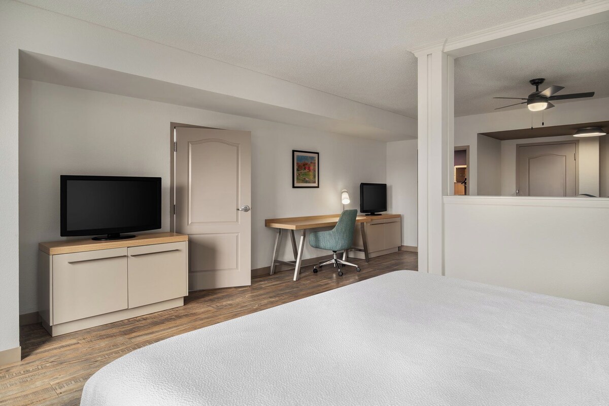 A bedroom with a bed, a desk with a computer, a television, and a door.