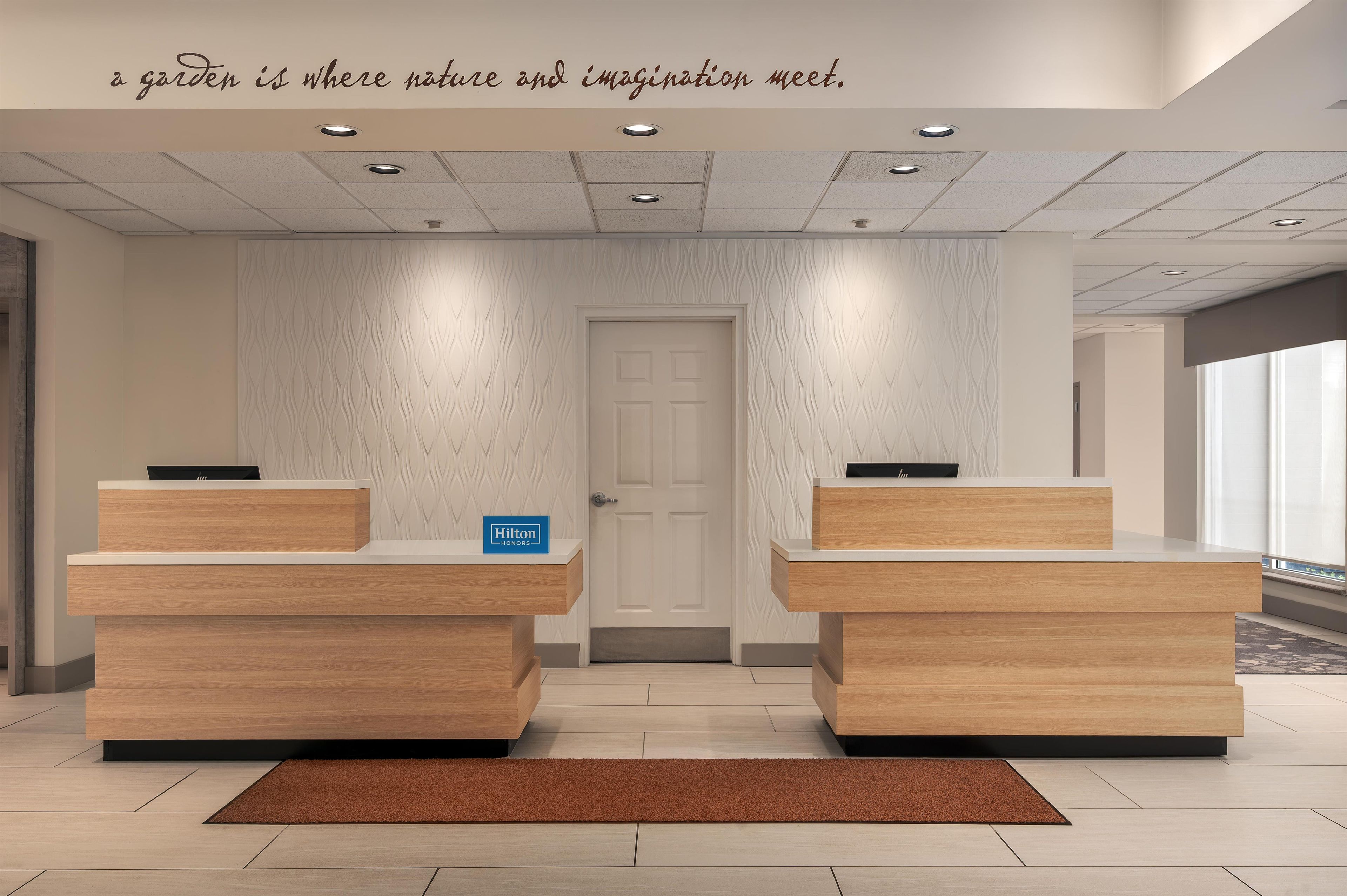 Un espace d’accueil d’hôtel comprenant deux comptoirs de réception, une porte et un mur orné d’un motif ondulé.