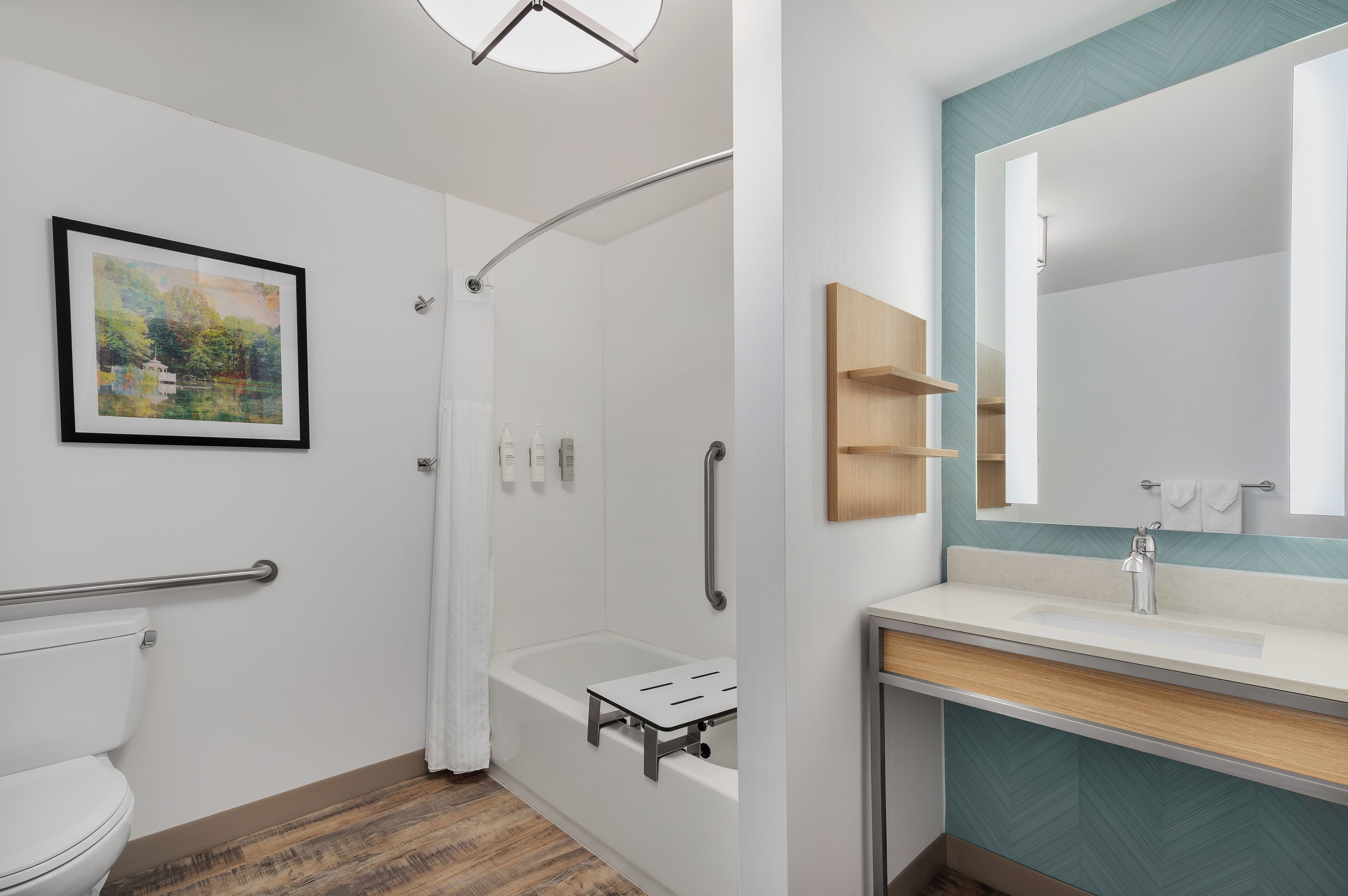 Un baño moderno con ducha, inodoro y lavamanos, que destaca por un revestimiento mural en patrón de espiga y un cuadro con paisaje enmarco.
