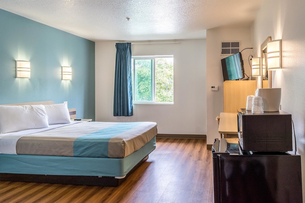 Hotelkamer met een bed, een bureau met stoel, een televisie en een raam met gordijnen.