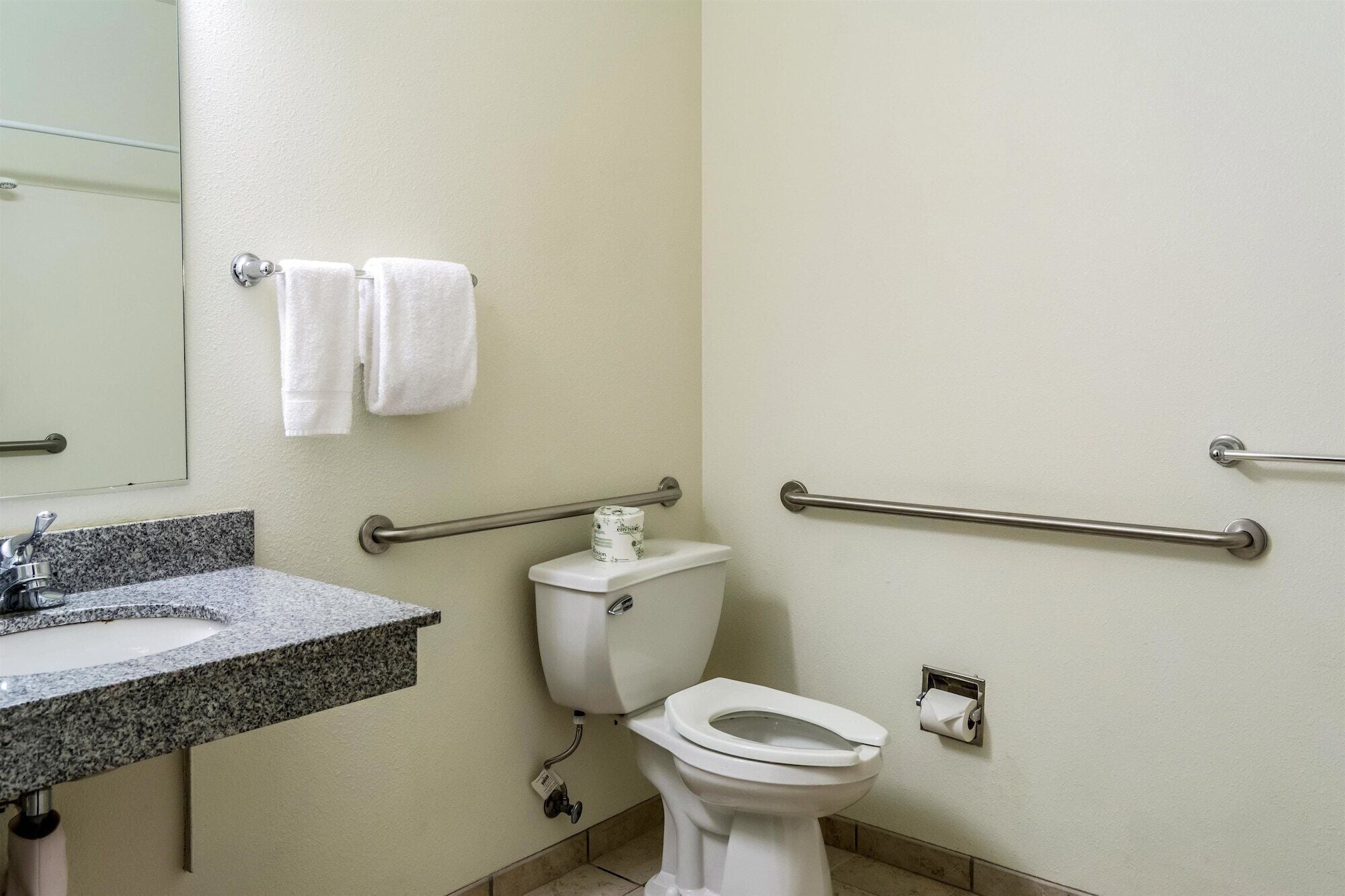 Un baño con lavamanos, inodoro y barras de apoyo.