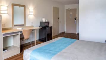 Ein Hotelzimmer mit Bett, Schreibtisch, Stuhl und einer Mikrowelle.