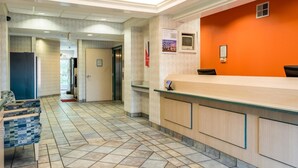 Zona de recepción de un hotel con un mostrador de check-in, un área de descanso con sillones estampados y piso de baldosas.