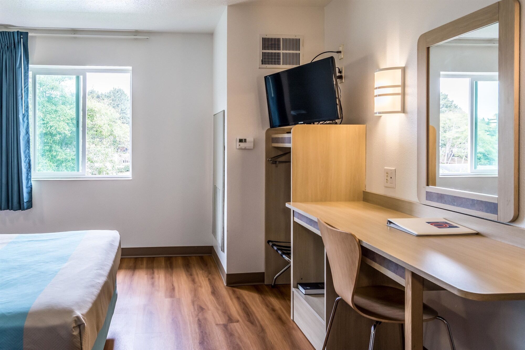 A hotel room with a bed, a desk with a chair, a television, and a window with curtains.