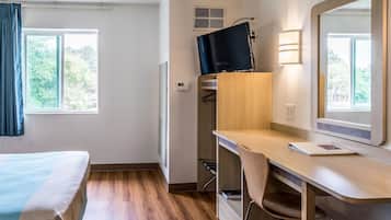 A hotel room with a bed, a desk with a chair, a television, and a window with curtains.
