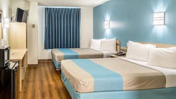 Quarto de hotel com duas camas, uma mesa de trabalho com computador, telefone e janela com cortinas azuis.