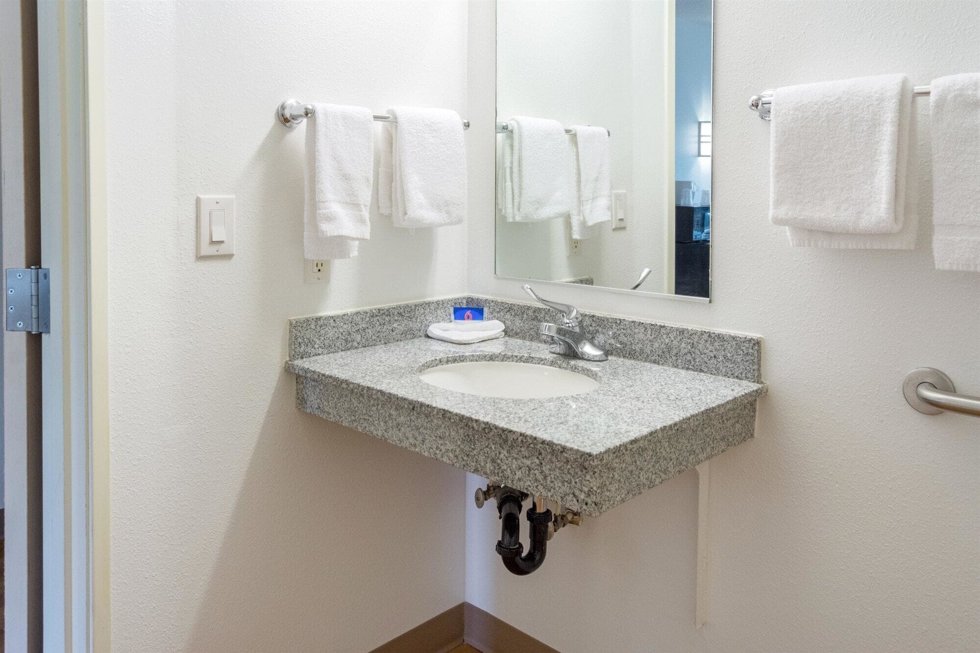 A bathroom with a granite sink, a mirror, and white towels hanging on a rack.