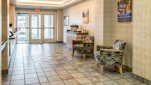Un vestíbulo de hotel con mostrador de recepción, dos sillones estampados, suelo de baldosas e iluminación empotrada en el techo.