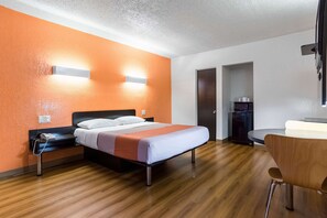 Une chambre d’hôtel comprenant un lit, une table de chevet et un bureau avec une chaise.