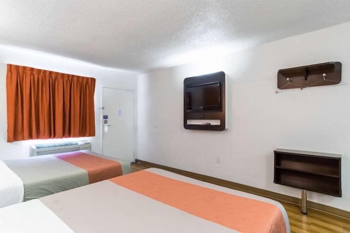 Una camera d'albergo con due letti, una televisione, un termosifone e uno scaffale.
