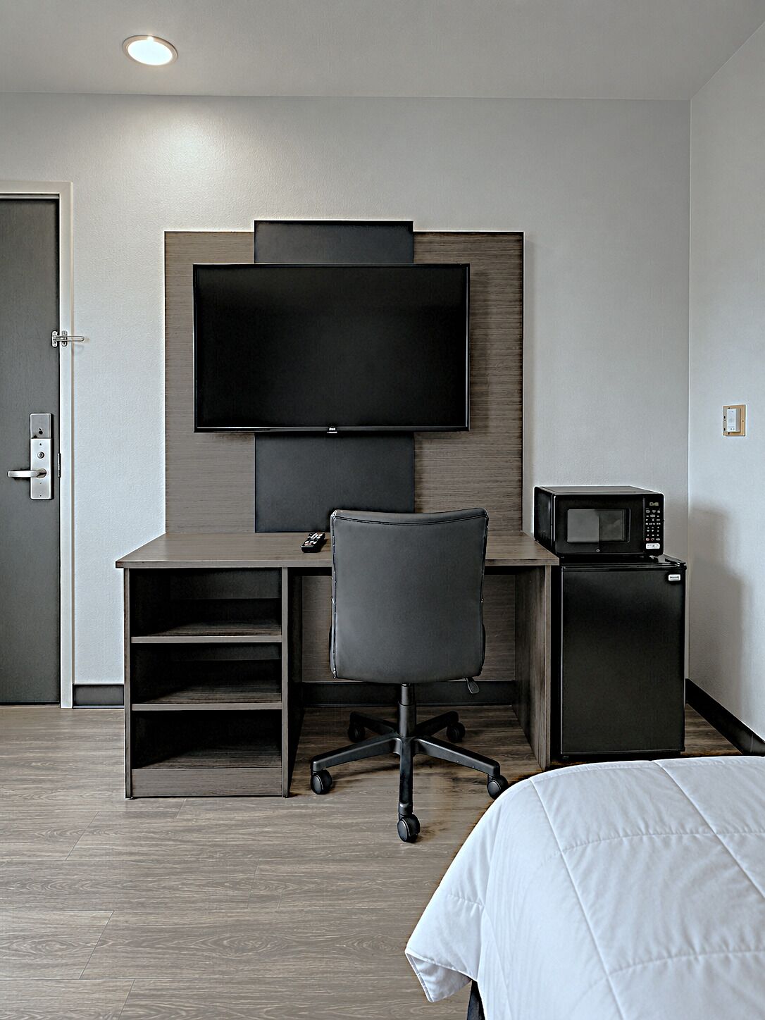 A hotel room with a bed, a desk with a chair, a television, and a microwave.