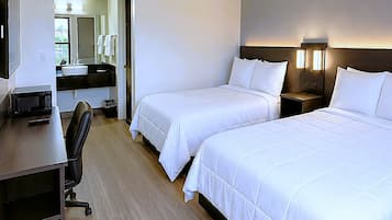 A hotel room with two beds, a desk, a chair, a microwave, a sink, and a mirror.