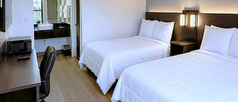 A hotel room with two beds, a desk, a chair, a microwave, a sink, and a mirror.
