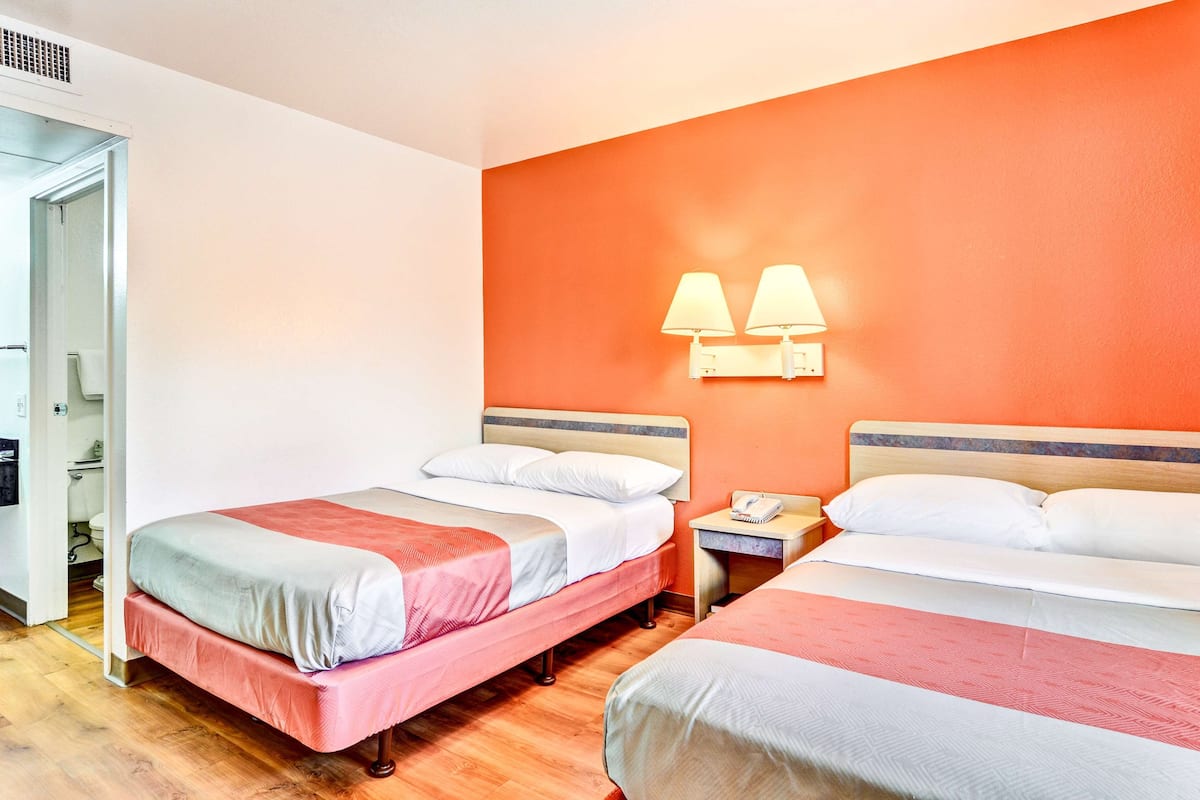 A hotel room with two beds, a wooden floor, and a bathroom visible through an open door.