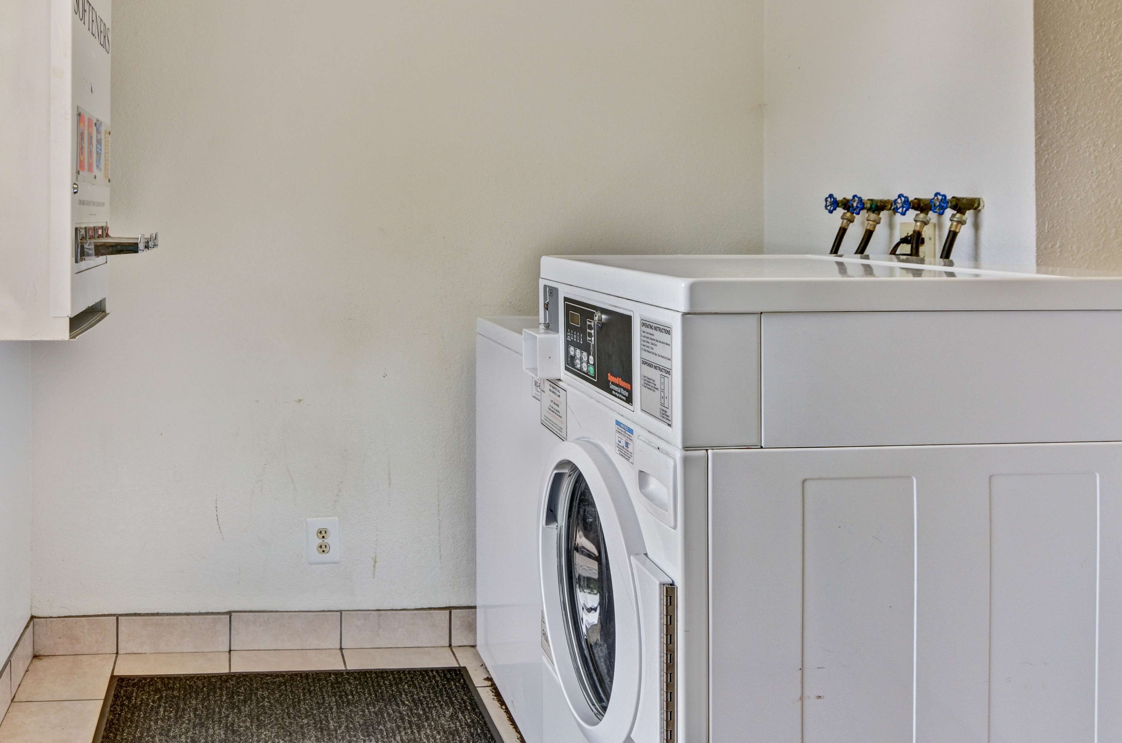 A laundry room with a front-loading washer and dryer, a wall-mounted utility cabinet, and a set of four water faucets on the wall.