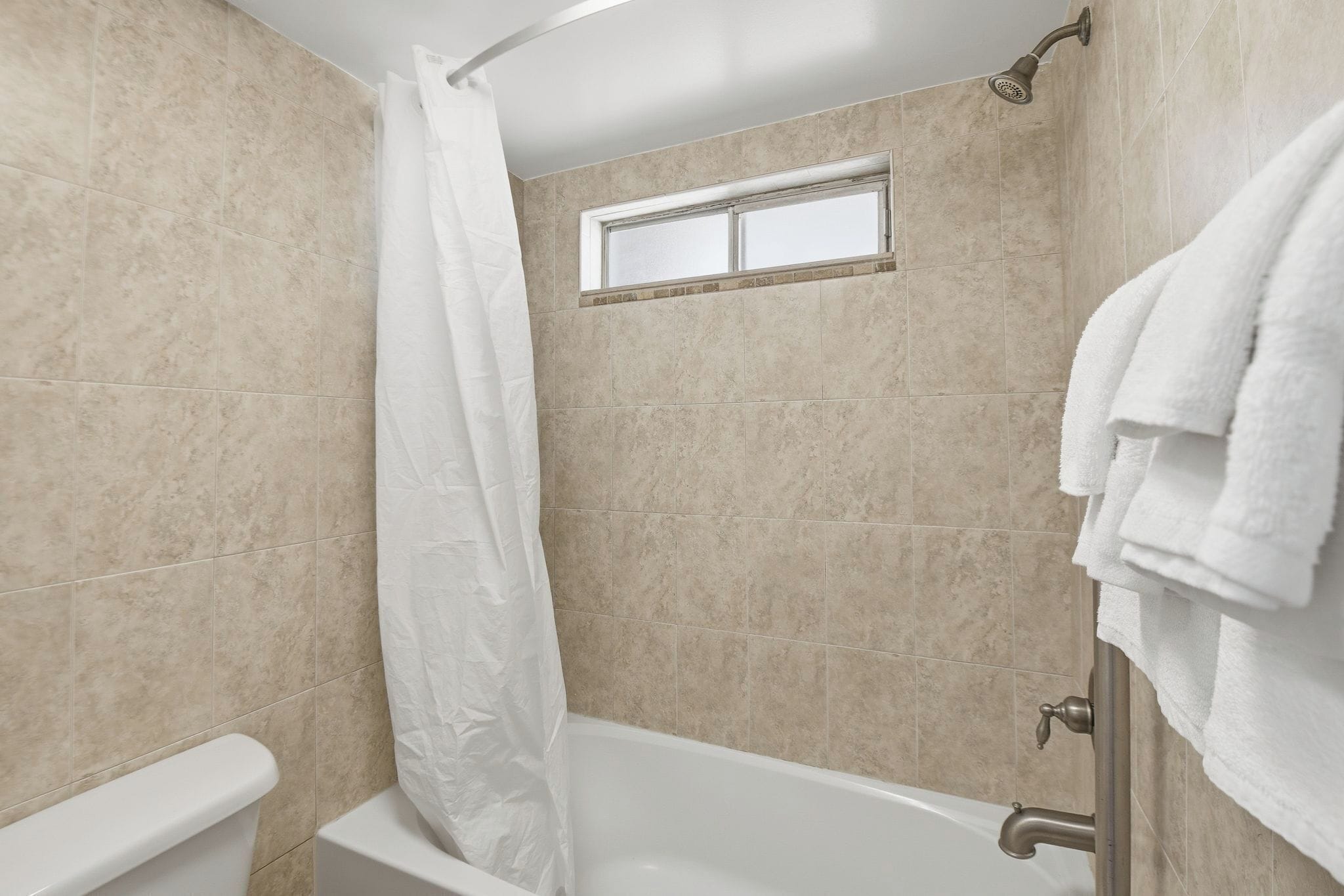 Un bagno con piastrelle color beige, una vasca da bagno bianca, una finestra e un box doccia.
